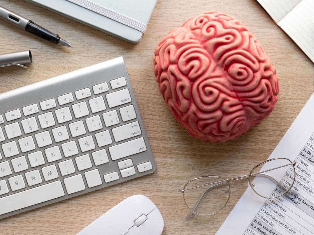 Mesa de atendimento neuropsicológico com modelo de cérebro, óculos, caderno e caneta, simbolizando o diagnóstico de TDAH e funções cognitivas.
